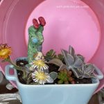 Une composition végétale de plantes succulentes avec une cassolette en céramique bleu ciel et un personnage clown acrobate