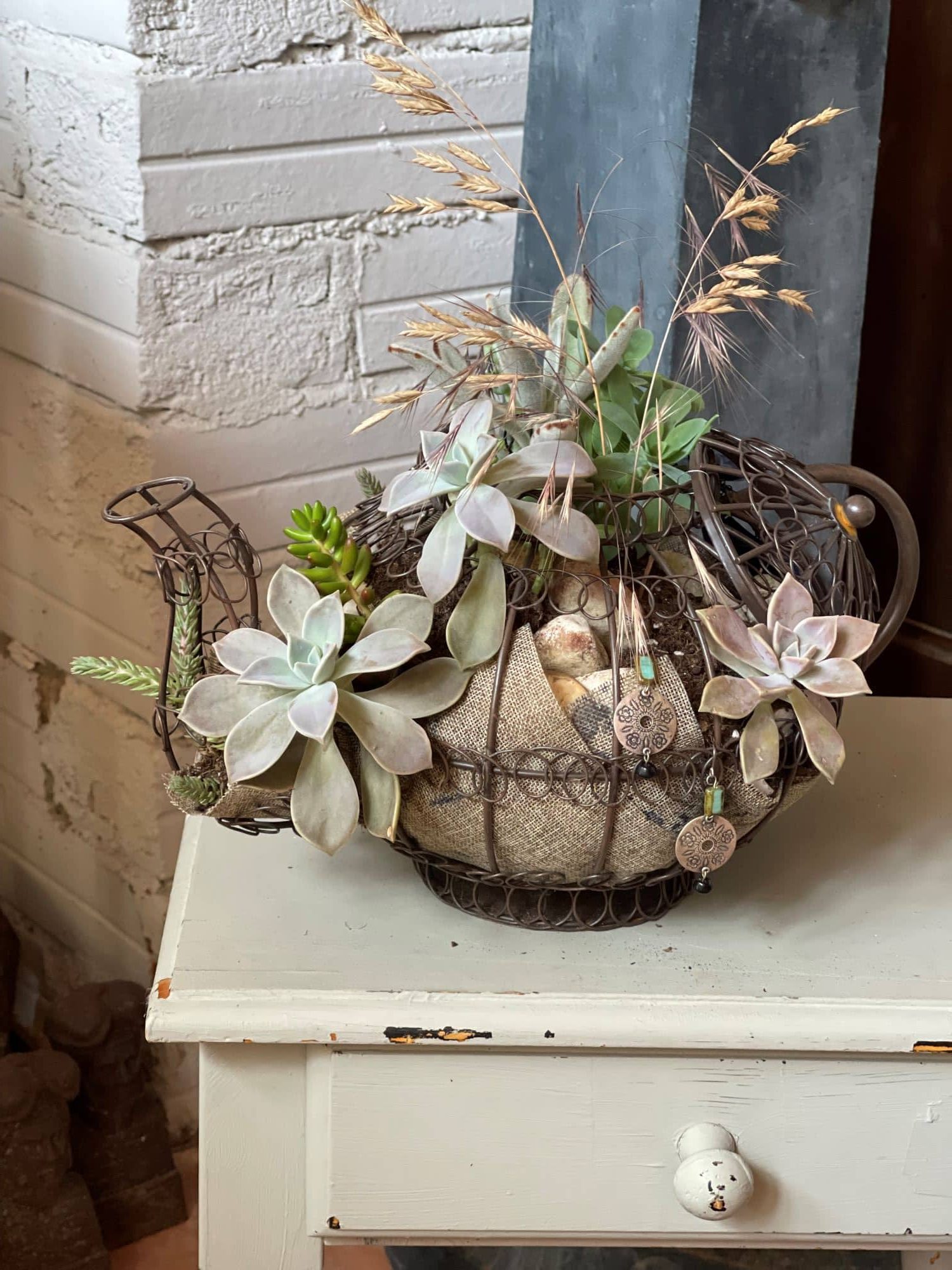 Une composition végétale de plantes succulentes avec une théière en fil métal et de la toile de jute
