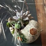 Une composition végétale de plantes succulentes avec un pot zoomorphe oiseau en céramique fleuri orange et vert