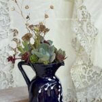 Une composition végétale de plantes succulentes dans un pichet en terre bleu marine vintage aux motif floral blanc