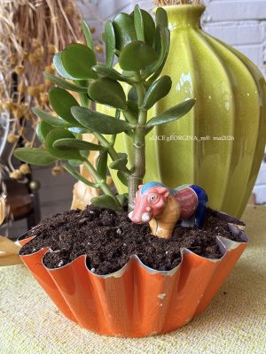 Composition végétale de plantes succulentes avec un moule à brioche en métal orange, patiné et un phacochère miniature en terre vernissé